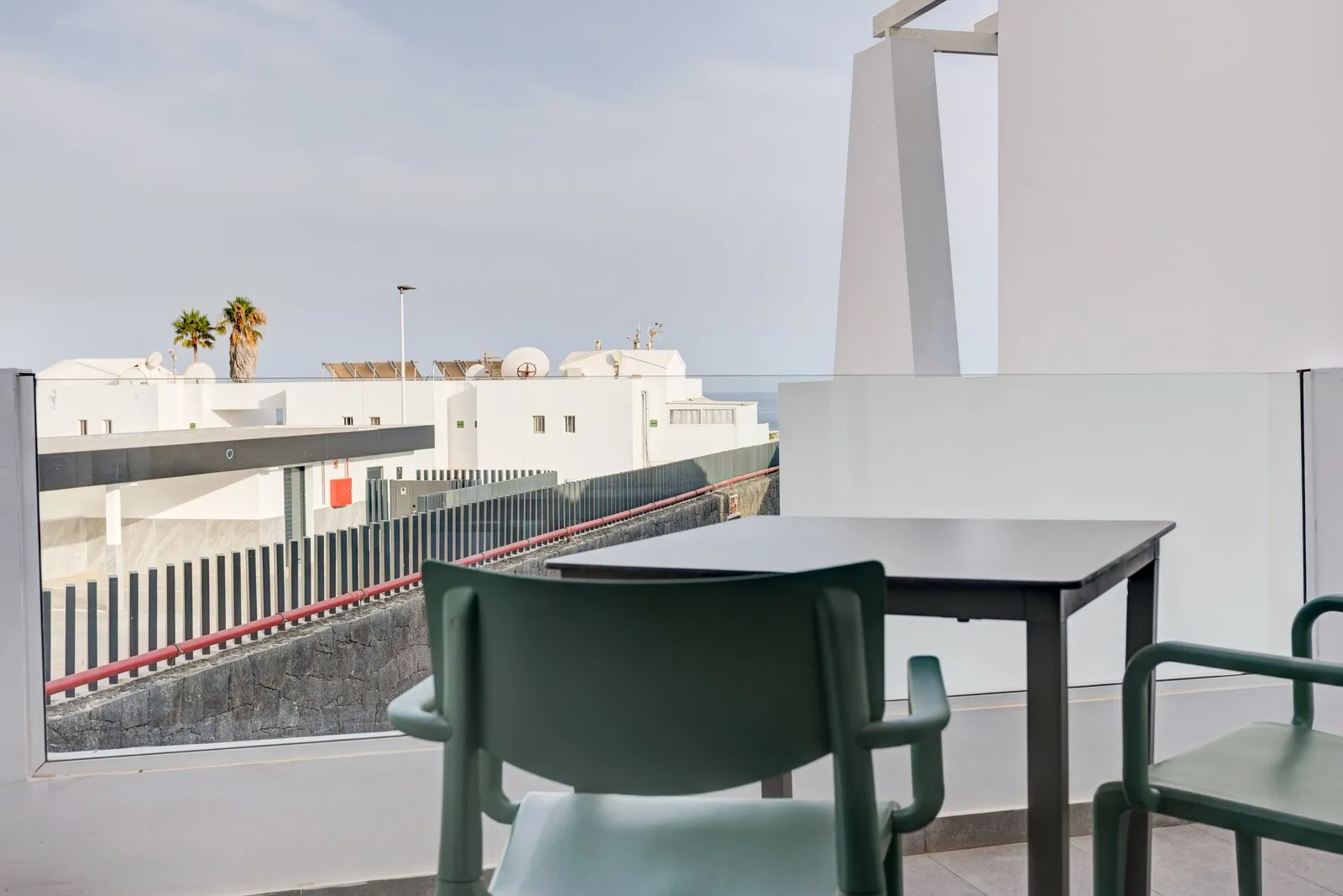 The terrace of apartment 206, with two green chairs, a table and a partial sea view