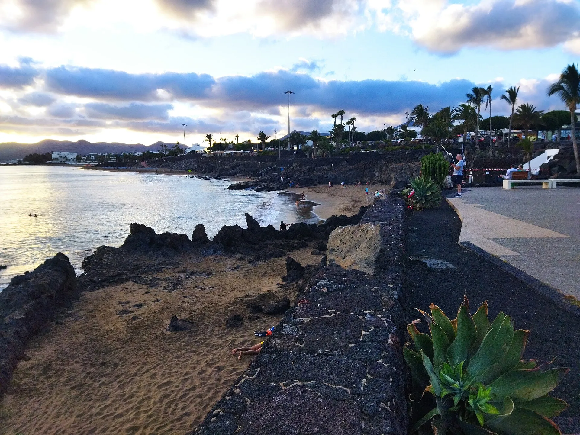 The end of Playa Grande at dusk, with lava rocks and the seafront promenade above the sand